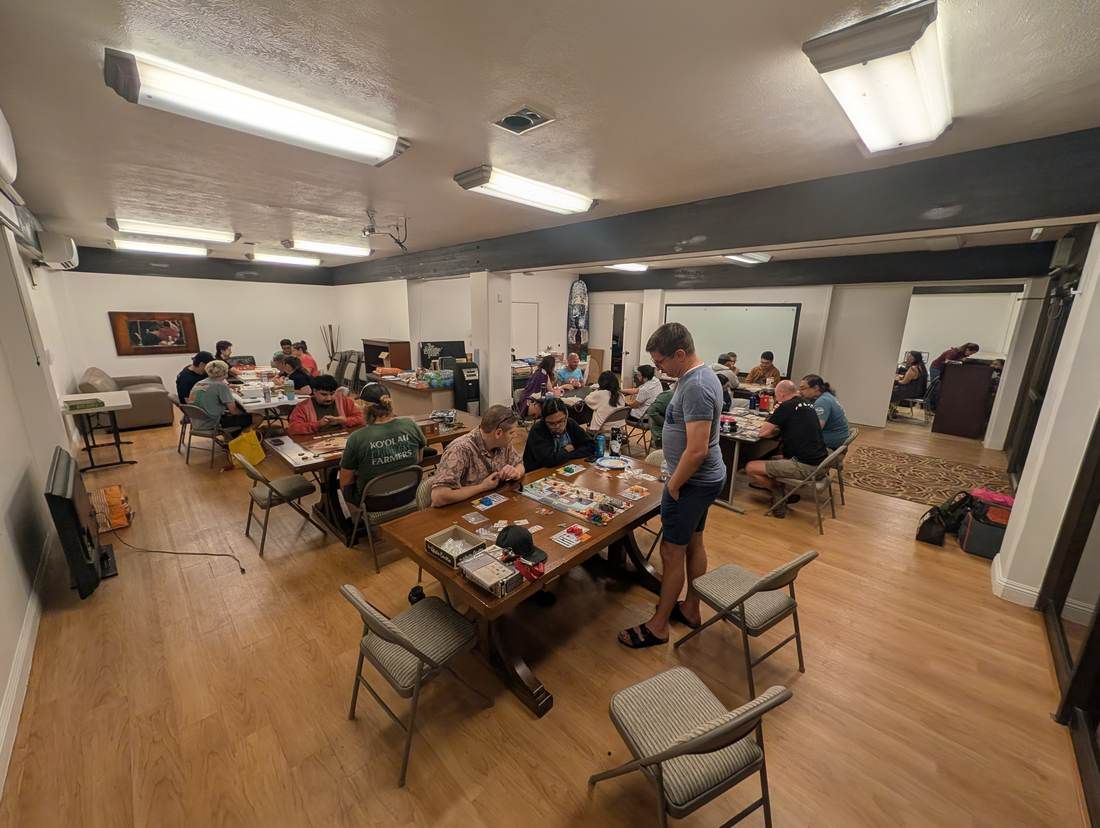 A community room full of tables of people playing board games at Monday game night
